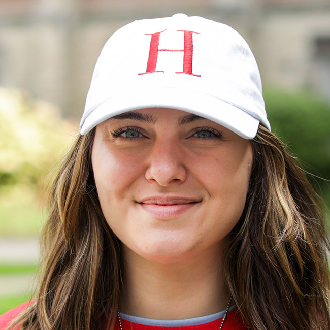 A smiling outdoor photo of Gillian Hunniset. She's wearing a Huron-branded ballcap and has long hair.